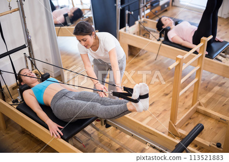 Pilates instructor helping woman exercising on reformer at gym Pilates instructor helping woman exercising on reformer at gym 113521883