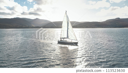 Slow motion yacht racing at ocean bay with highlang island coast aerial. Sun reflect at sailboat 113523630