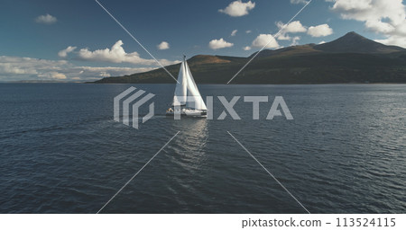 Slow motion of yacht, wind blows to sail at ocean aerial. Mountain island of Arran, Scotland, Europe Slow motion of yacht, wind blows to sail at ocean aerial. Mountain island of Arran, Scotland, Europe 113524115