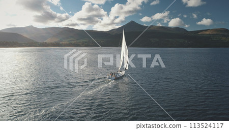 Slow motion of yacht, wind blows to sail at ocean aerial. Mountain island of Arran, Scotland, Europe Slow motion of yacht, wind blows to sail at ocean aerial. Mountain island of Arran, Scotland, Europe 113524117