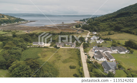 Green mountain valley village aerial. Scottish nature landscape of town at sea lake, castle ruins 113524202