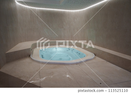 Luxurious indoor jacuzzi with beige marble tiles and bubbling water, creating a relaxing and elegant ambiance. Curved ceiling with soft lighting adds to the tranquil atmosphere. 113525110