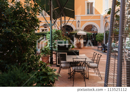 Luxurious outdoor seating area with lush plants and umbrella shaded tables at a hotel in Rome. Classic Italian architecture and cozy lighting create a tranquil retreat. 113525112