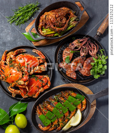 Set table with seafood dishes - cooked crabs, tiger shrimps, grilled octopus and squids on cast iron pan. 113525212