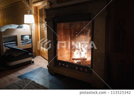 Cozy indoor scene with fireplace framed by stone surround and mantel. Rustic bunk bed and floor lamp add charm. Located in a domestic setting, possibly rural or mountainous. 113525342