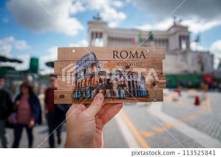 Hand holding Colosseum postcard in Rome, Italy. ROMA and COLOSSEO on the postcard, blurred background of outdoor area with historic building and people. Hand holding Colosseum postcard in Rome, Italy. ROMA and COLOSSEO on the postcard, blurred background of outdoor area with historic building and people. 113525841