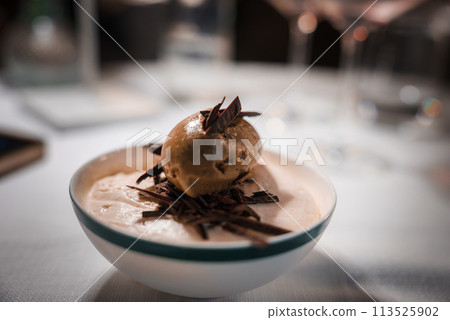 Indulge in a luxurious dessert at an upscale fine dining restaurant, featuring a creamy base, chocolate shavings, and a golden chocolate orb. Aesthetic elegance in an exquisite setting. Indulge in a luxurious dessert at an upscale fine dining restaurant, featuring a creamy base, chocolate shavings, and a golden chocolate orb. Aesthetic elegance in an exquisite setting. 113525902