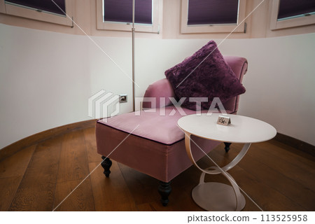 Luxury room corner with pink armchair, purple cushion, and white table in Zermatt, Switzerland. Intimate, elegant decor with diffused lighting for relaxation. 113525958