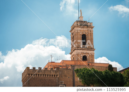 Historic brick tower rising above a fortified building, possibly a bell tower or part of a religious structure. European architecture, could be in Italy. 113525995