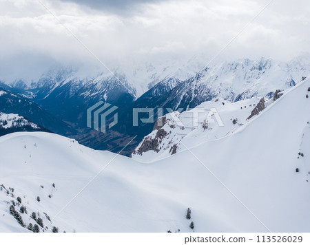 Aerial view of Verbier, Switzerland's snow covered slopes and peaks, perfect for skiing and snowboarding. Sparse vegetation and clouds enhance the alpine charm and fun. 113526029