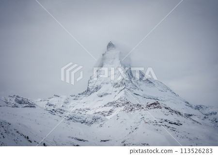This image captures the Matterhorn's serene grandeur in the Swiss Alps by Zermatt, showing its iconic peak in clouds above snow covered slopes, suggesting alpine activities in a winter wonderland. This image captures the Matterhorn's serene grandeur in the Swiss Alps by Zermatt, showing its iconic peak in clouds above snow covered slopes, suggesting alpine activities in a winter wonderland. 113526283