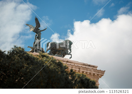 Statues of a winged figure and a bull on a classical pedestal, surrounded by lush greenery under a blue sky. Possibly in Europe or with European influences. 113526321
