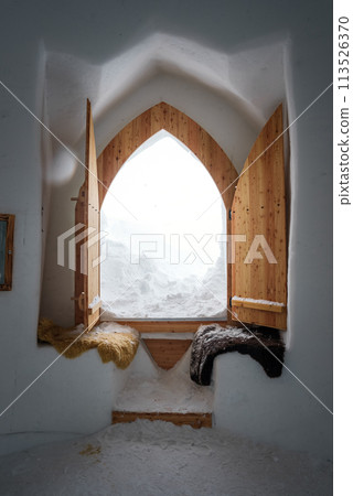 Interior of a snow covered room in Zermatt ski resort. Walls and floor made of snow, wooden door open to snow landscape. Cozy, rustic atmosphere with fur blankets. Interior of a snow covered room in Zermatt ski resort. Walls and floor made of snow, wooden door open to snow landscape. Cozy, rustic atmosphere with fur blankets. 113526370
