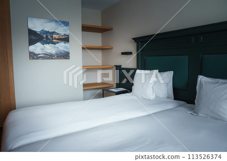Luxury hotel room in Zermatt, Switzerland. Features include a large bed, dark green headboard, wooden desk, and alpine artwork. Muted colors and elegant decor create a peaceful atmosphere. 113526374