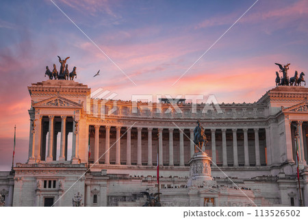 A majestic view of Altare della Patria, or National Monument to Victor Emmanuel II, in Rome, Italy. White marble facade, statues, and Italian flag under a clear blue sky. A majestic view of Altare della Patria, or National Monument to Victor Emmanuel II, in Rome, Italy. White marble facade, statues, and Italian flag under a clear blue sky. 113526502