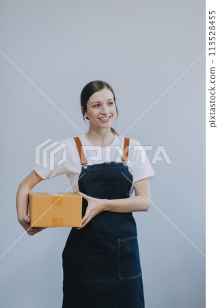 Smiling Asian woman in casual clothes holding a cardboard box mockup while standing against an isolated white background. shipping business concept 113528455