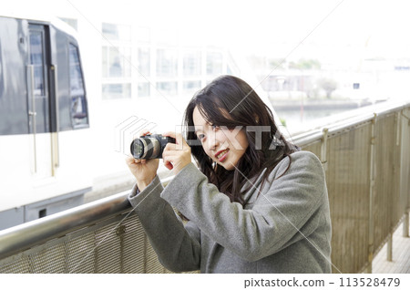 A woman photographing a train from a station platform 113528479