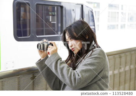 A woman photographing a train from a station platform A woman photographing a train from a station platform 113528480