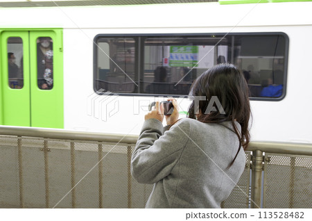 A woman photographing a train from a station platform A woman photographing a train from a station platform 113528482