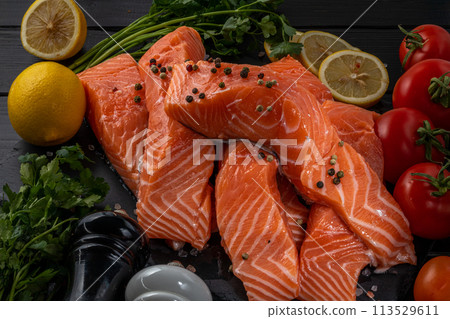 Fresh raw salmon fillet with cooking ingredients, herbs and lemon on black slate 113529611