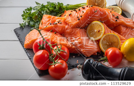 Fresh raw salmon fillet with cooking ingredients, herbs and lemon on black slate 113529629