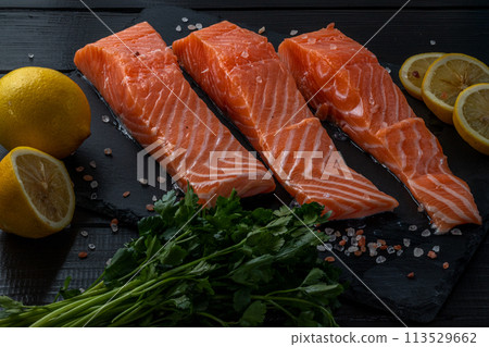 Fresh raw salmon fillet with cooking ingredients, herbs and lemon on black slate 113529662