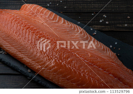 Fresh raw salmon fillet with cooking ingredients, herbs and lemon on black slate 113529796