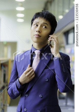 A young man wearing a double-breasted suit standing on the phone, vertical position, photo courtesy of Ariake College of Education and Arts 113530456