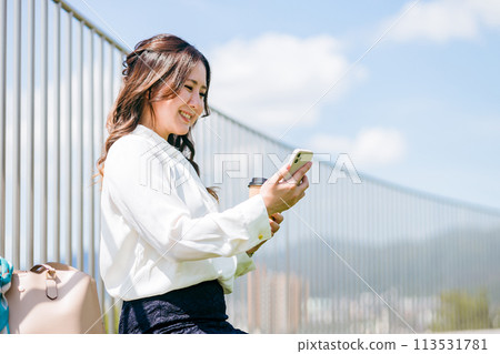 A young businesswoman drinking coffee on the rooftop and looking at her smartphone A young businesswoman drinking coffee on the rooftop and looking at her smartphone 113531781
