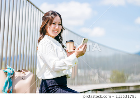 A young businesswoman drinking coffee on the rooftop and looking at her smartphone 113531785