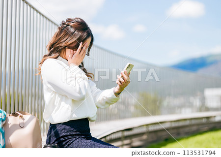 Businesswoman looking at her smartphone on the rooftop (despair, trouble, shock, mistake, failure, what should I do) Businesswoman looking at her smartphone on the rooftop (despair, trouble, shock, mistake, failure, what should I do) 113531794
