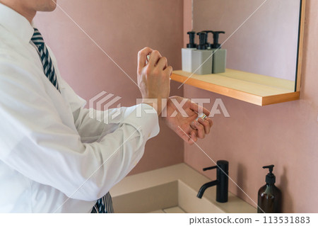 Young Asian businessman in a suit applying perfume to his wrist before going to work in the morning (men's cologne, men's perfume) 113531883
