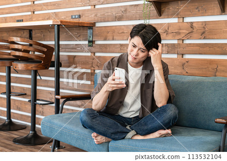A young man relaxing at home playing with his smartphone (troubled, replying, email, worried, confused) 113532104