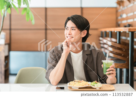 Young man drinking green smoothie while eating lunch at a cafe (enzyme/detox/dietary fiber/health food) 113532887