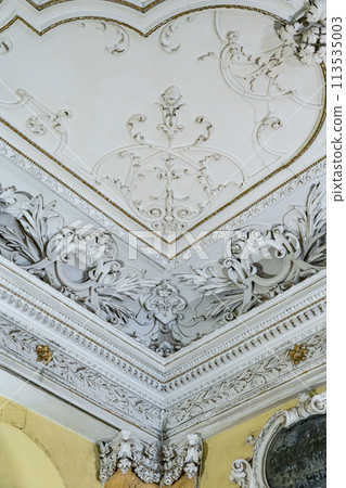 Round antique vintage decorative clay stucco relief molding with floral ornaments on white ceiling in abstract classical style interior Round antique vintage decorative clay stucco relief molding with floral ornaments on white ceiling in abstract classical style interior 113535003