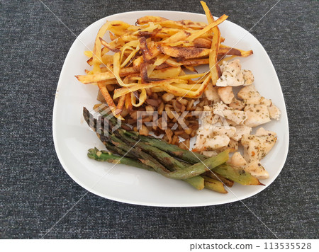 Homemade grilled chicken with french fries, eggplant and grilled asparagus, served on a white plate 113535528