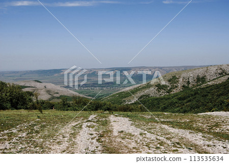 A settlement can be seen in the distance between two hills.Mountainous area of the Crimean peninsula, a populated area is visible in the plain. 113535634
