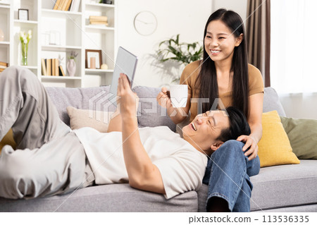 Happy Asian Couple Relaxing and Using Tablet at Home Happy Asian Couple Relaxing and Using Tablet at Home 113536335