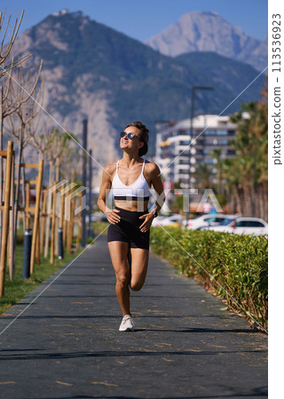 Female runner running at morning in city park. Healthy fitness woman jogging outdoors. Mountains in 113536923