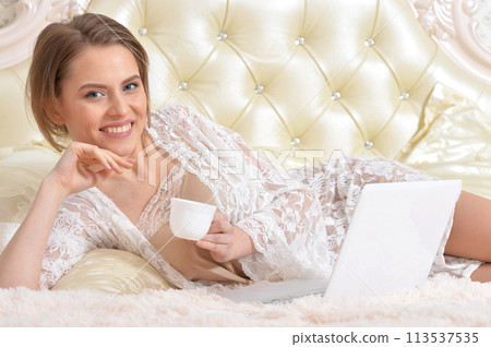 Portrait of young beautiful woman with coffee cup on bed 113537535