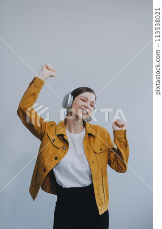 The beautiful emotional European brown-haired woman with healthy clean skin, charming smile, dressed in casual light clothes, listens and enjoys music on headphones with tablet on a white background. The beautiful emotional European brown-haired woman with healthy clean skin, charming smile, dressed in casual light clothes, listens and enjoys music on headphones with tablet on a white background. 113538021