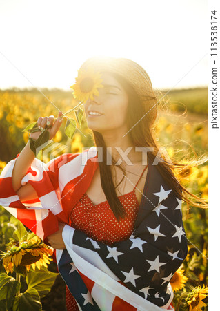 Beautiful girl in hat with the American flag in a sunflower field. 4th of July. Fourth of July. Freedom 113538174