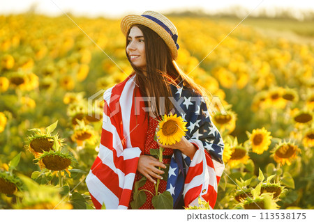 Beautiful girl in hat with the American flag in a sunflower field. 4th of July. Fourth of July. Freedom 113538175