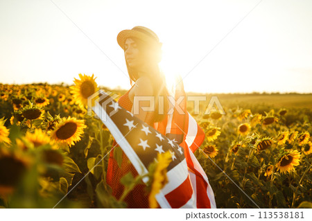 Beautiful girl in hat with the American flag in a sunflower field. 4th of July. Fourth of July. Independence Day. Beautiful girl in hat with the American flag in a sunflower field. 4th of July. Fourth of July. Independence Day. 113538181