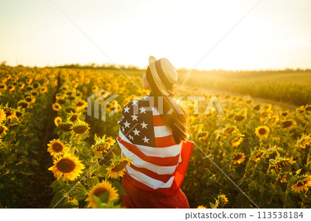 Beautiful girl in hat with the American flag in a sunflower field. 4th of July. Fourth of July. Independence Day. 113538184