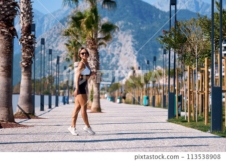 fit girl in sportswear goes to morning workout at park, carrying yoga mat holds bottle of water 113538908