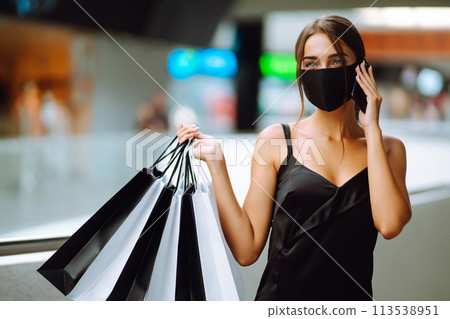 Young woman in protective black medical mask with shopping bags talking on a mobile phone in the mall. 113538951