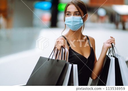 Fashionable woman in protective medical mask with shopping bags walking in the mall. Covid-19. Fashionable woman in protective medical mask with shopping bags walking in the mall. Covid-19. 113538959