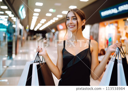 Elegant brunette woman in black dress enjoying shopping in the mall. Spring Style. Consumerism. 113538984