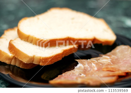 Food ingredients like slices of meat and bread served on black plate 113539569